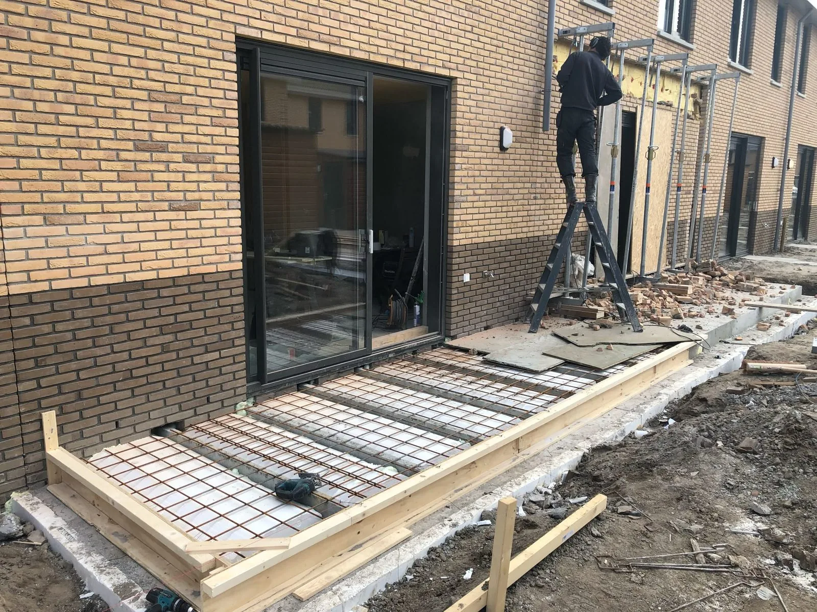 Een aanbouw in aanbouw: de wapening voor de vloer ligt klaar naast een nieuwe schuifpui